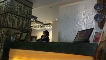 A reception desk with a receptionist, a wall with a circular pattern, and a clock displaying New York and Manila times.