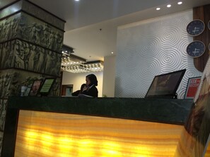 Un mostrador de recepción con una recepcionista, una pared con diseño circular y un reloj que muestra la hora en Nueva York y Manila.