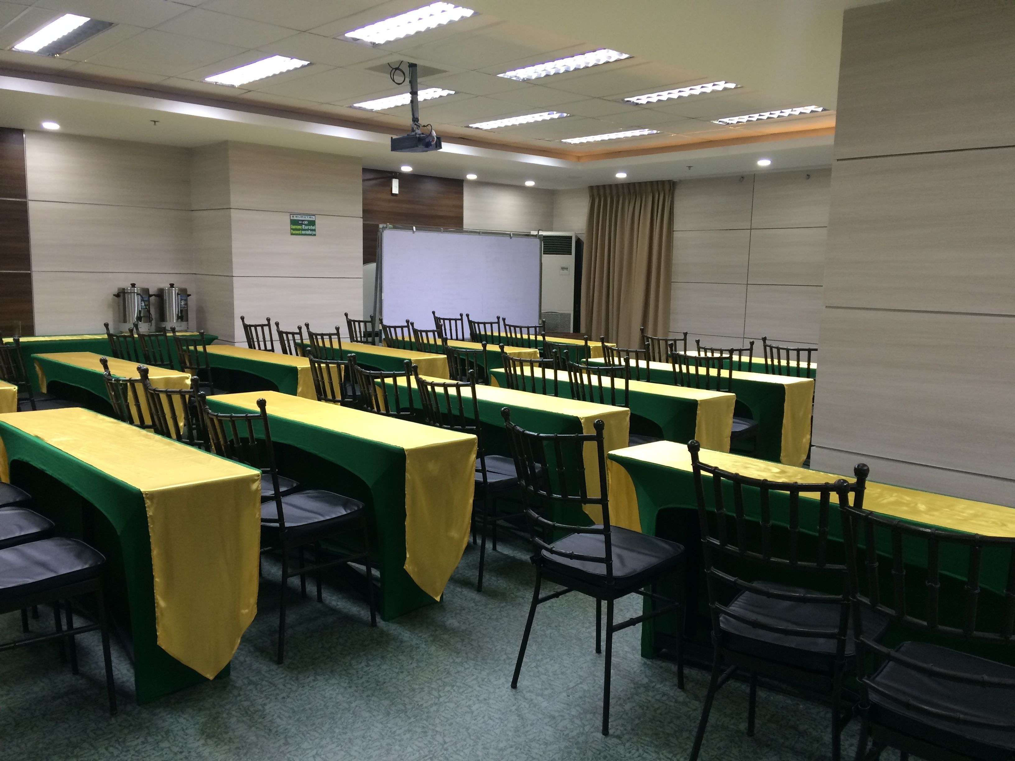A conference room with rows of tables and chairs, a projector, and a whiteboard.