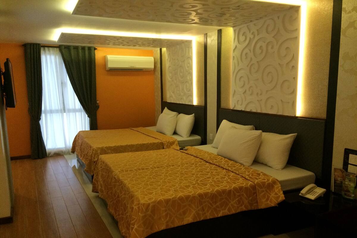 A hotel room with two beds, a desk, a chair, an air conditioning unit, and a telephone on a nightstand.