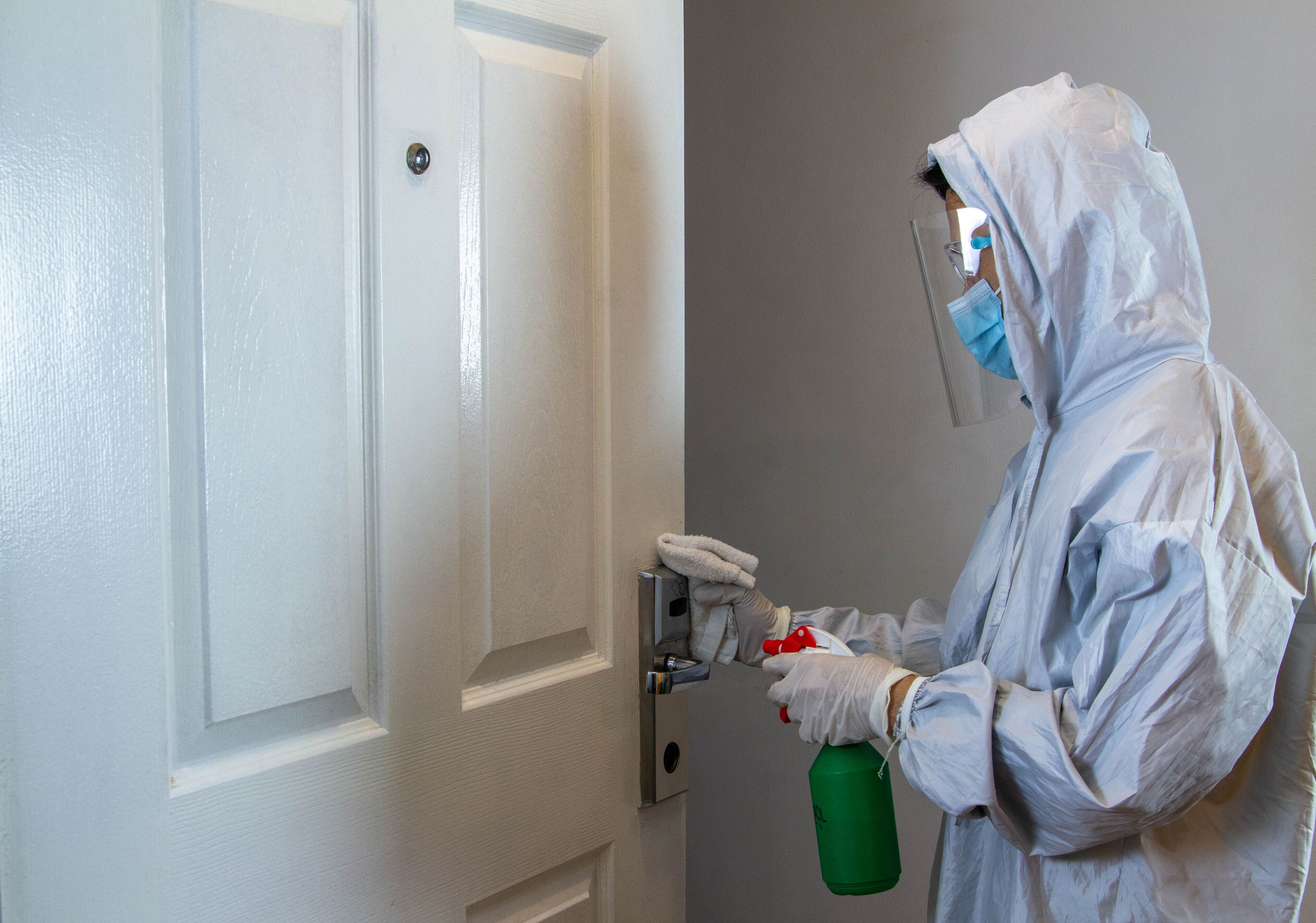 A person in a protective suit spraying a door with a green bottle.