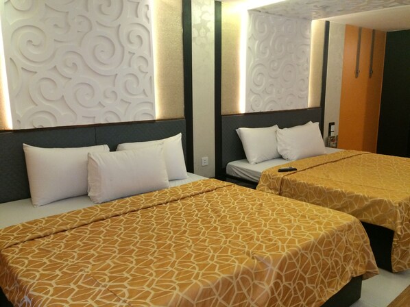 Habitación de hotel con dos camas, cada una con una colcha estampada y almohadas blancas. La habitación presenta un diseño moderno con paneles decorativos en la pared y un cabecero de madera.