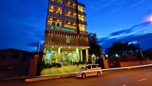 Un hotel de varios pisos con fachada moderna, entrada bien iluminada y un camino de acceso con portón.