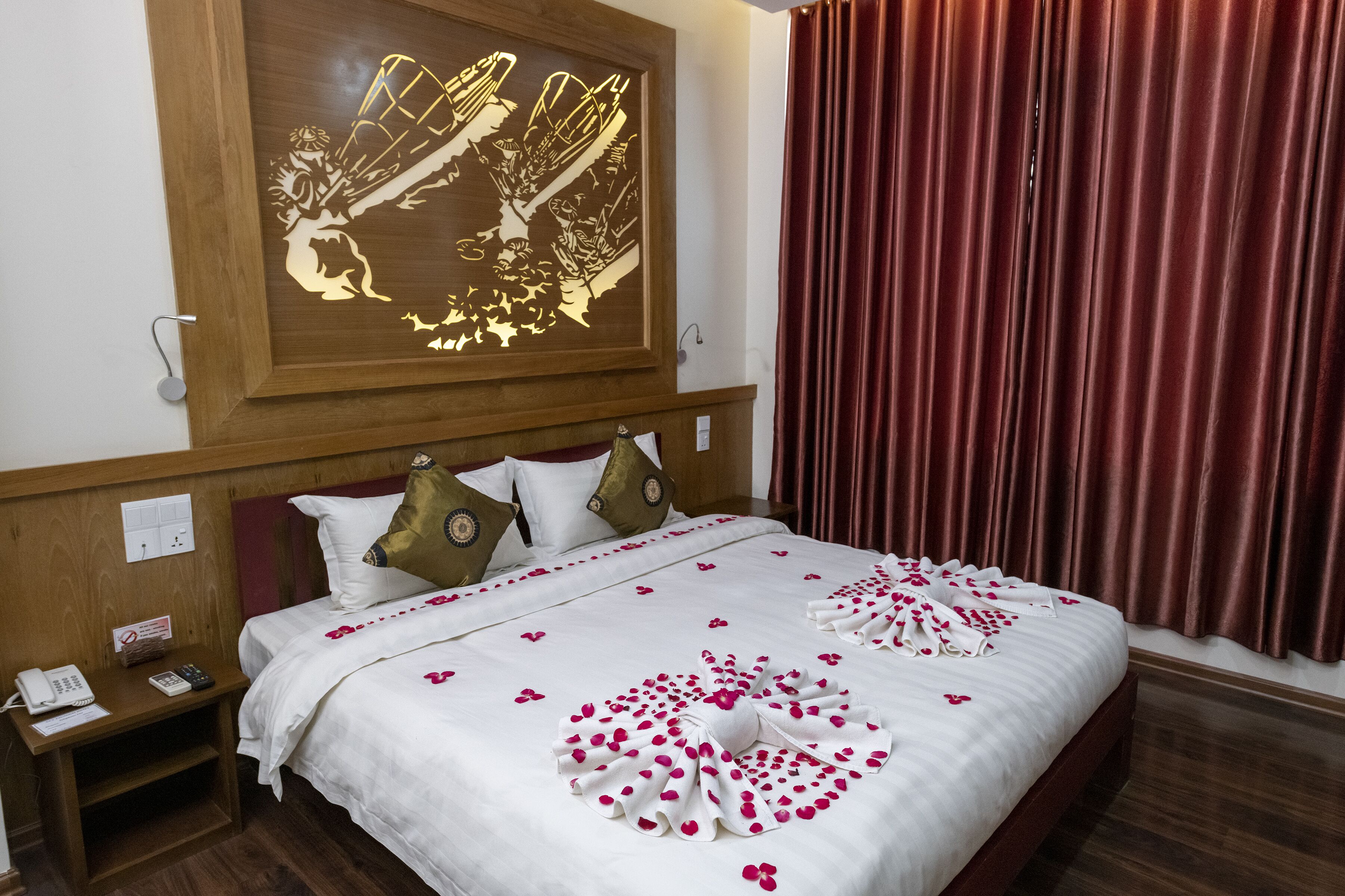 A neatly made bed with white bedding and pink floral arrangements, a wooden headboard, and a wall-mounted artwork.