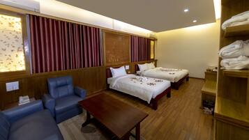 A hotel room with two beds, a sofa, a wooden table, and a wardrobe.