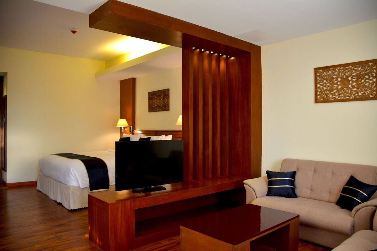 A hotel room with a bed, a TV, a sofa, and a wooden partition.