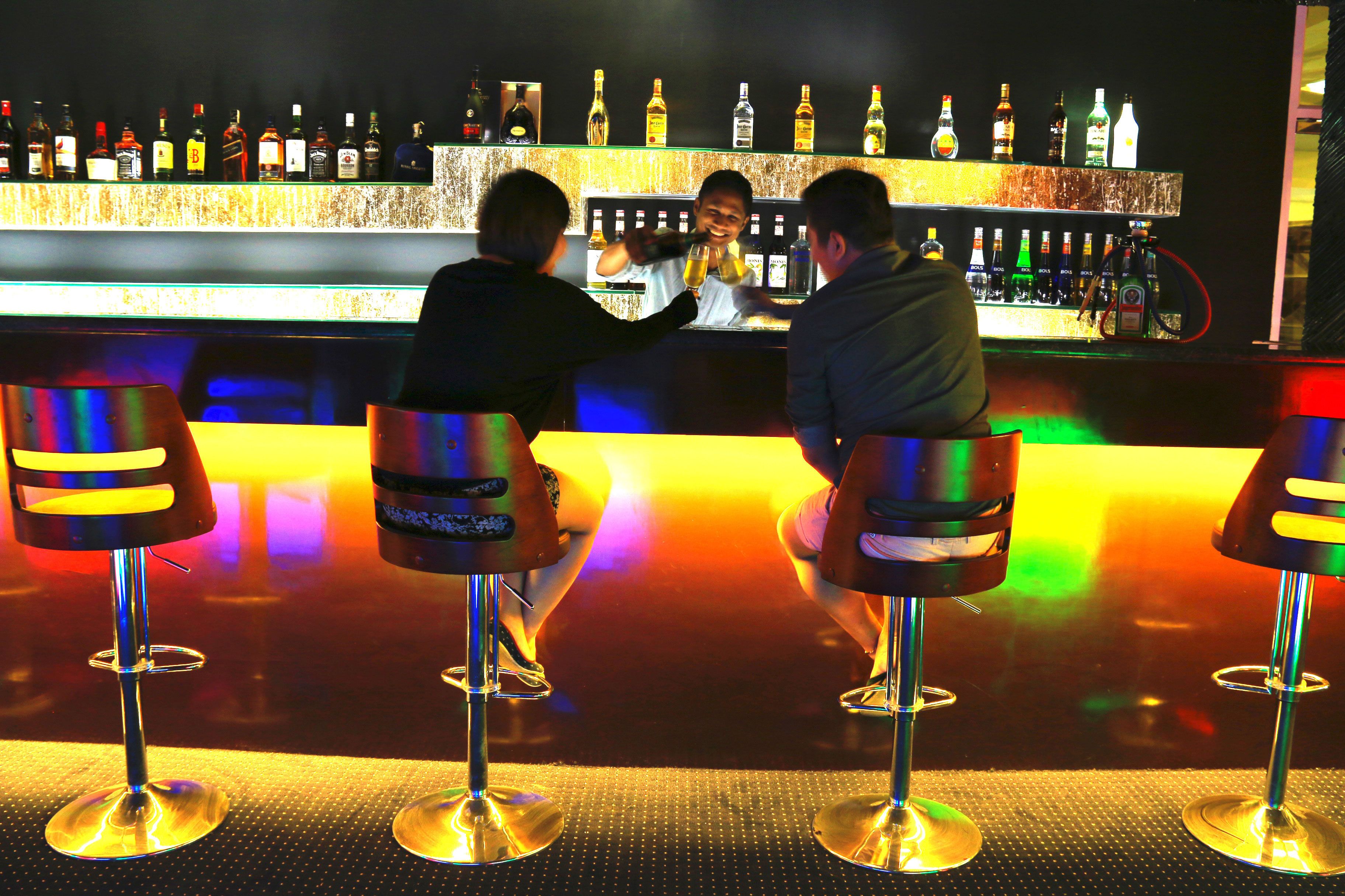 Een bar met krukken en een plank met drankflessen.