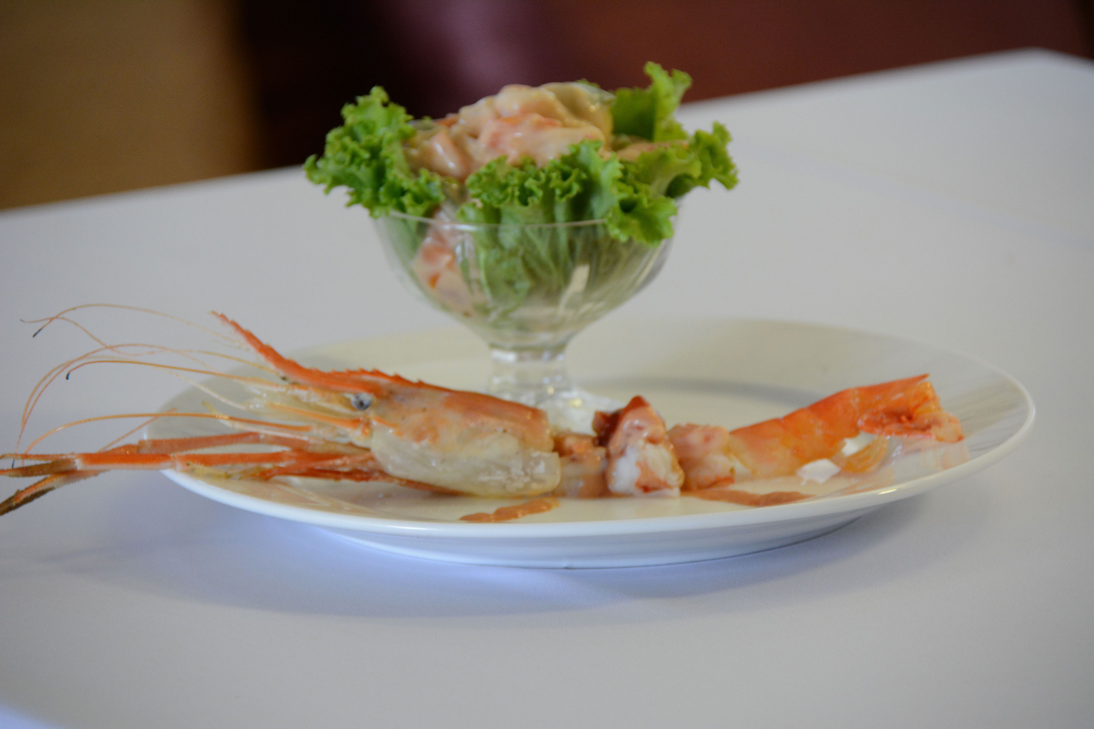 A plate with a cooked lobster and a glass bowl containing salad.