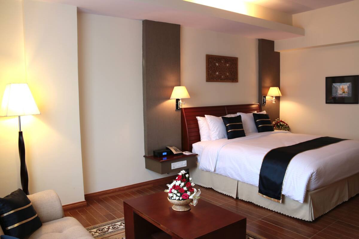A hotel room with a large bed, two bedside lamps, a nightstand, and a decorative flower arrangement.