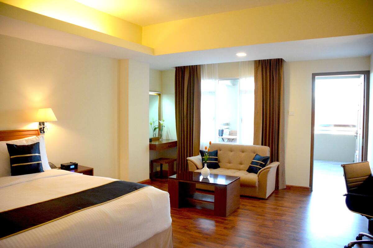 A hotel room with a large bed, a sofa, a coffee table, and a desk.