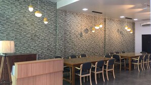 Ein Konferenzraum mit einem langen Holztisch, Stühlen, einer strukturierten Wand und Pendelleuchten.