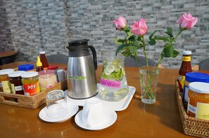 A table with a stainless steel coffee pot, a pitcher of detox water, a glass of water, and various condiments. - Check In @ Downtown Yangon (Yangon)