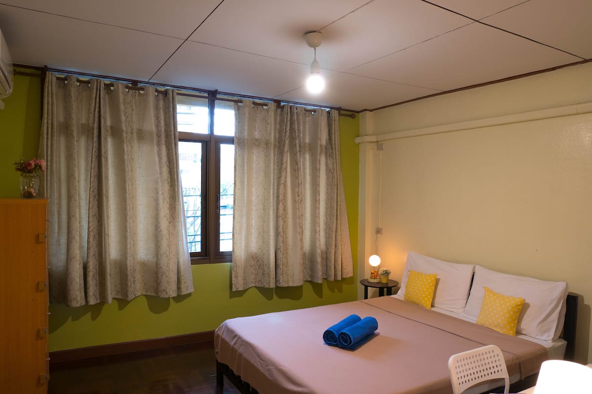 A room with a bed, a chair, a nightstand, and a window with curtains.
