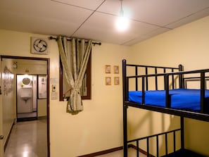 A room with a bunk bed, a bathroom with a shower, and a hallway leading to another room.