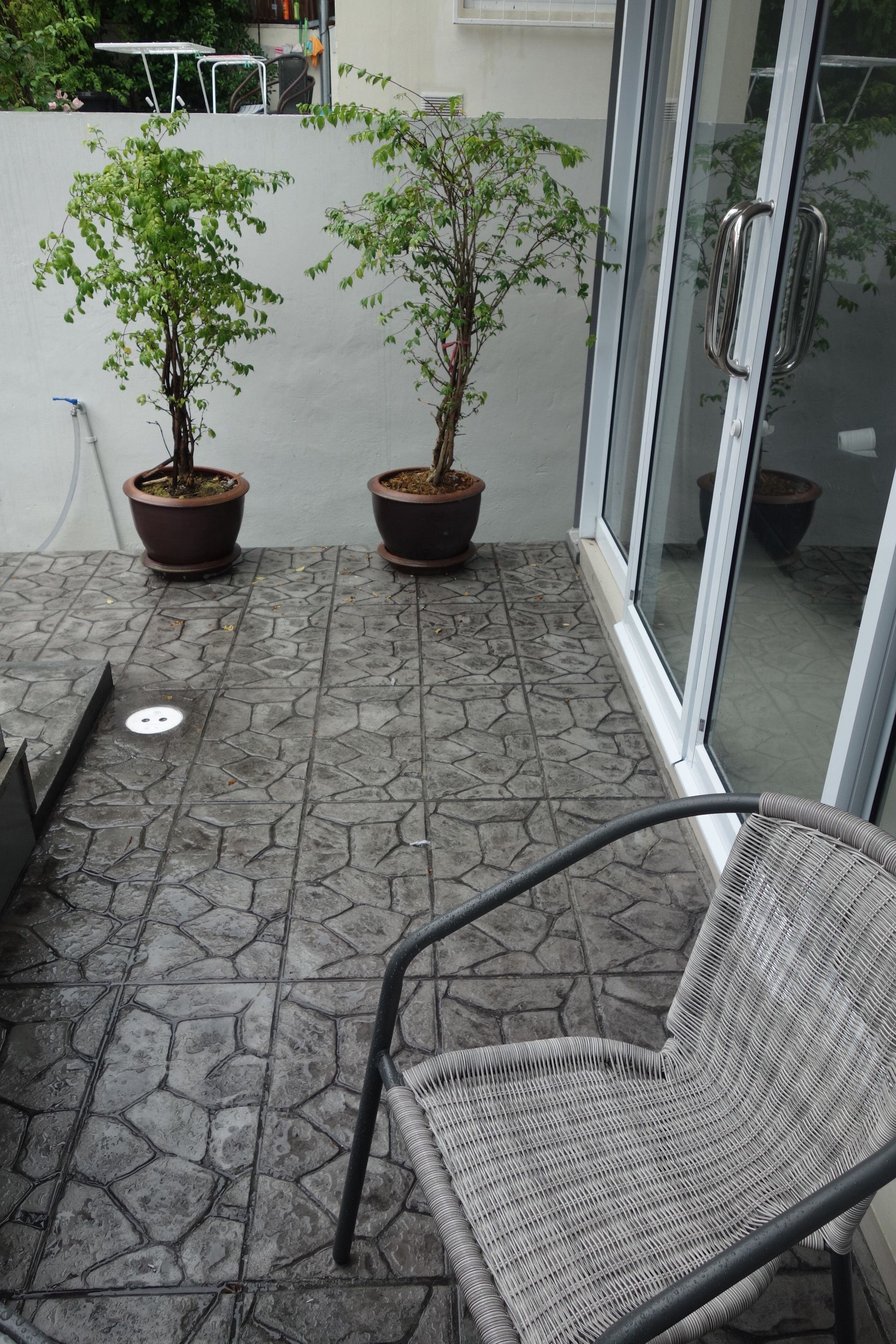 Una terrazza con due piante in vaso, una sedia e una porta in vetro.