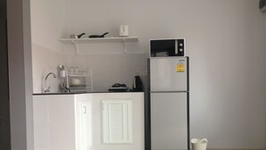 Cuina compacta amb armaris blancs, un refrigerador negre i un microones a la part superior.