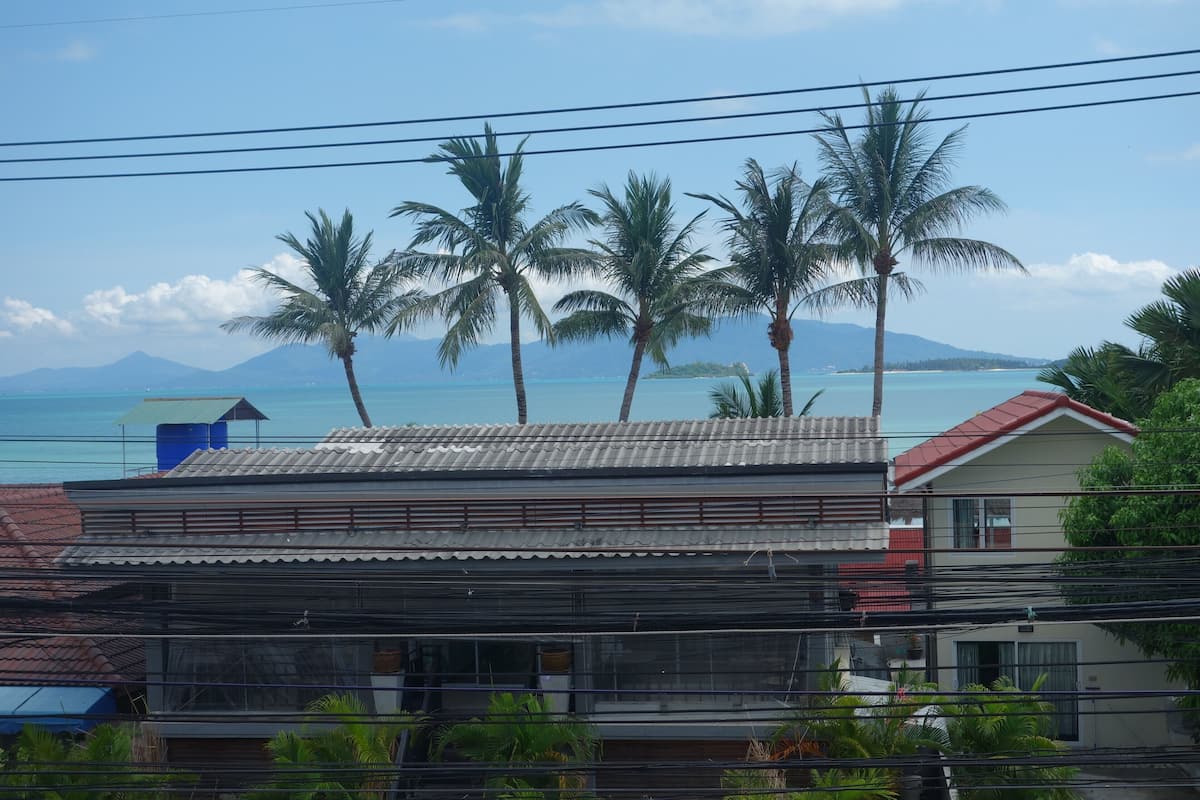 Un bâtiment situé sur la côte, avec un toit rouge, entouré de palmiers et offrant une vue sur l’océan.
