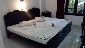 Ein ordentlich bezogenes Bett mit weißer Bettdecke und Kissen, ein Nachttisch mit Telefon und Taschentüchern sowie ein Fenster mit Blick auf Grünflächen.