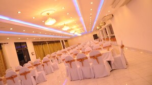 A banquet hall with rows of white chairs with orange sashes, a chandelier, and recessed ceiling lights. - Sarathchandra Tourist Guest House (Embilipitiya)