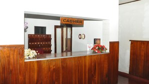 A wooden reception desk with a 'CASHIER' sign, a calendar, and a flower arrangement. - Sarathchandra Tourist Guest House (Embilipitiya)