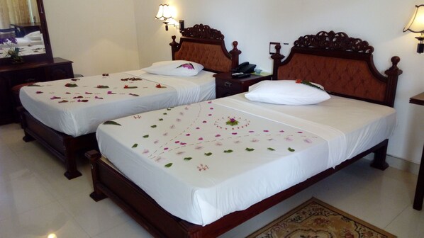 Two single beds with white linens and floral decorations, wooden headboards, bedside tables with lamps, and a mirror on the left. - Sarathchandra Tourist Guest House (Embilipitiya)