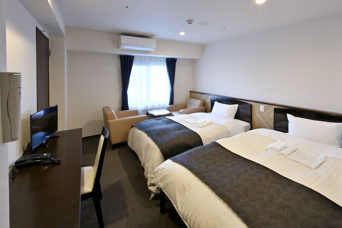 A hotel room with two beds, a desk with a television, and a chair.