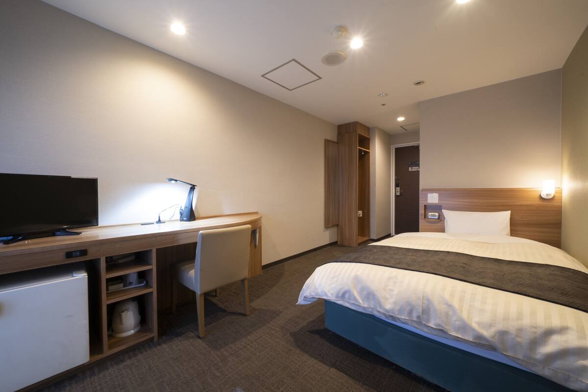 A hotel room with a bed, a desk with a computer, a television, and a wardrobe.