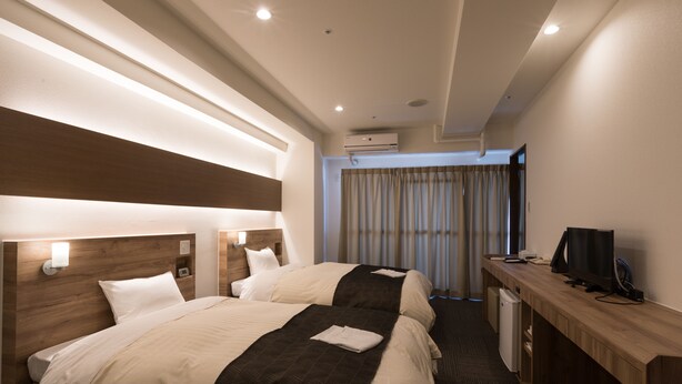 A hotel room with two beds, a desk with a television, and an air conditioning unit.