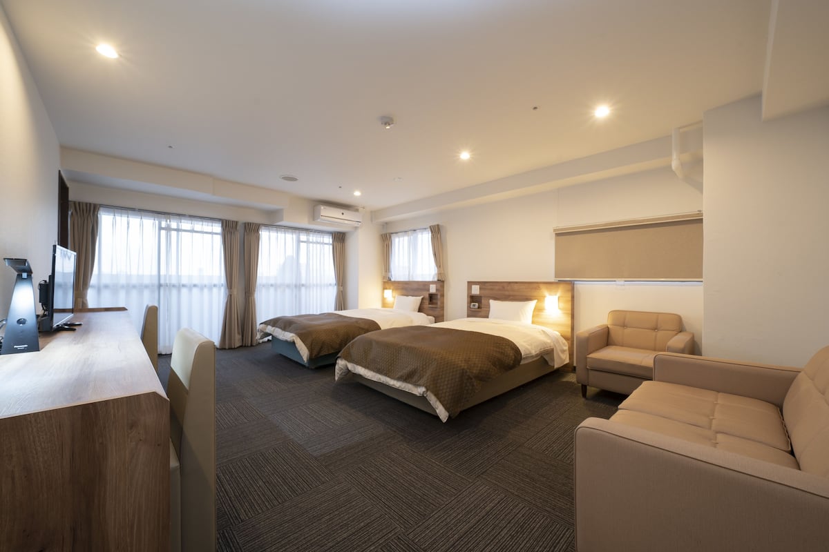 A hotel room with two beds, a desk, a chair, and a sofa.