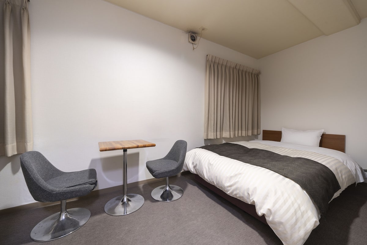 A hotel room with a bed, two armchairs, a small table, and a window with curtains.