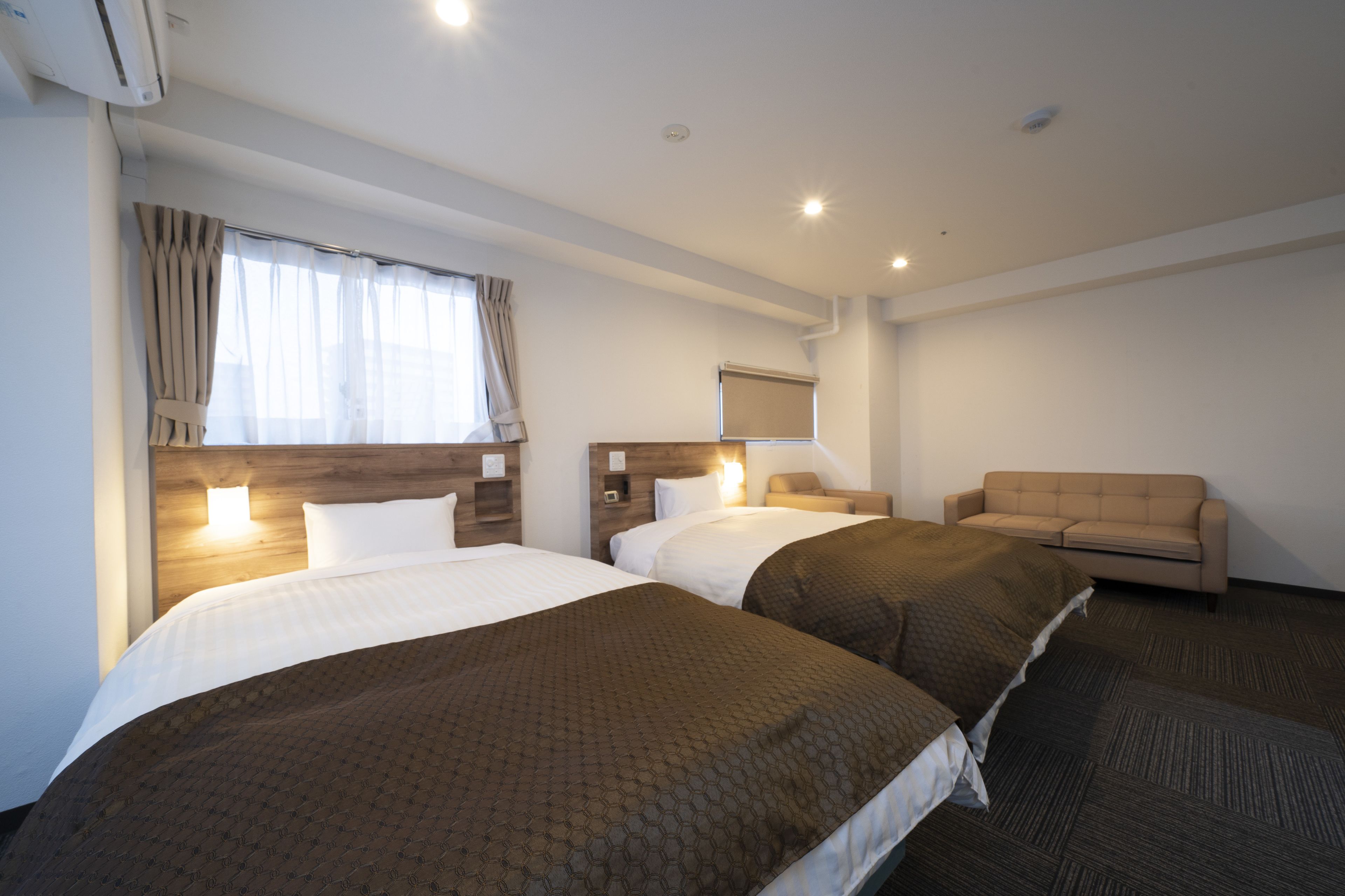 A hotel room with two beds, a sofa, a flat-screen TV, and a window with curtains.