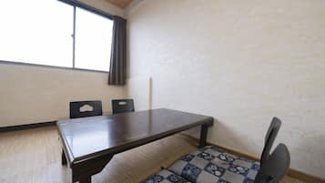 A room with a wooden table, two chairs, a patterned sofa, a window with curtains, and a textured wall.