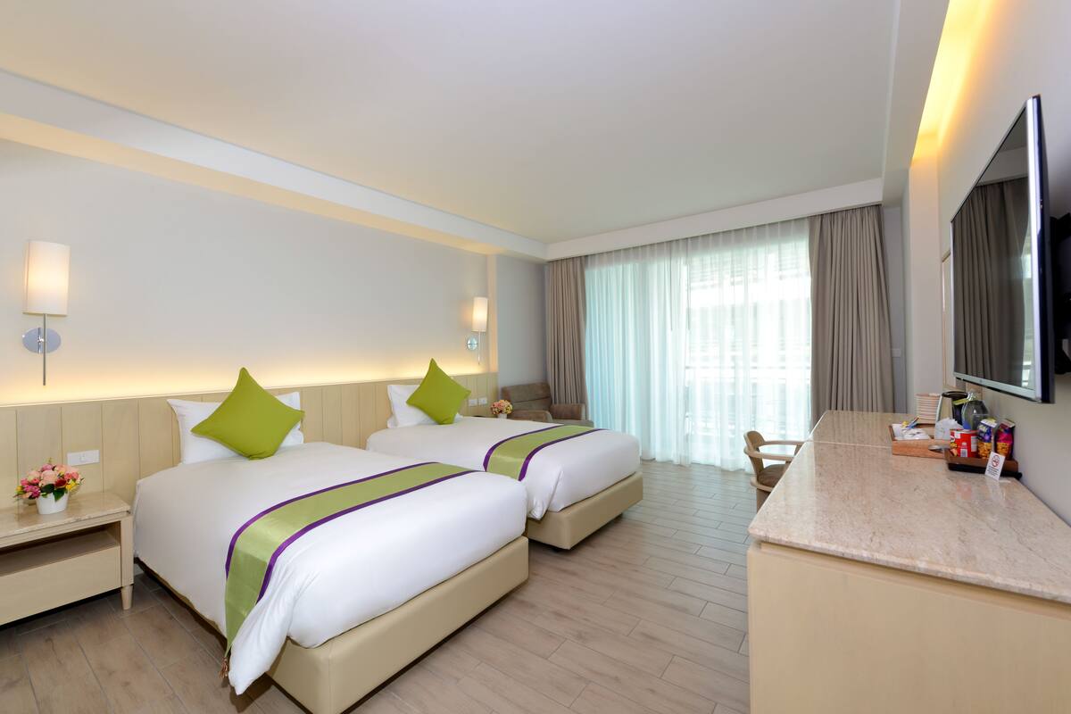 A hotel room with two beds, a desk, a TV, and a window with curtains.