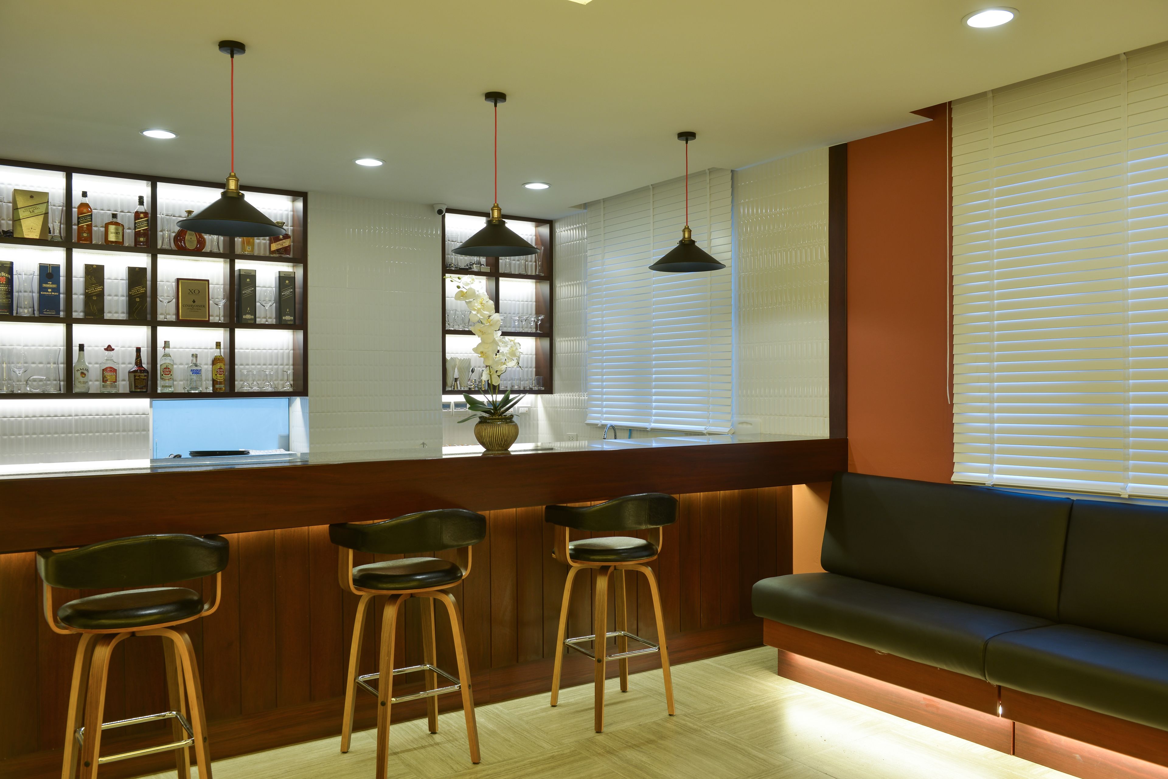 A bar area with wooden stools, a bar counter, and pendant lighting.