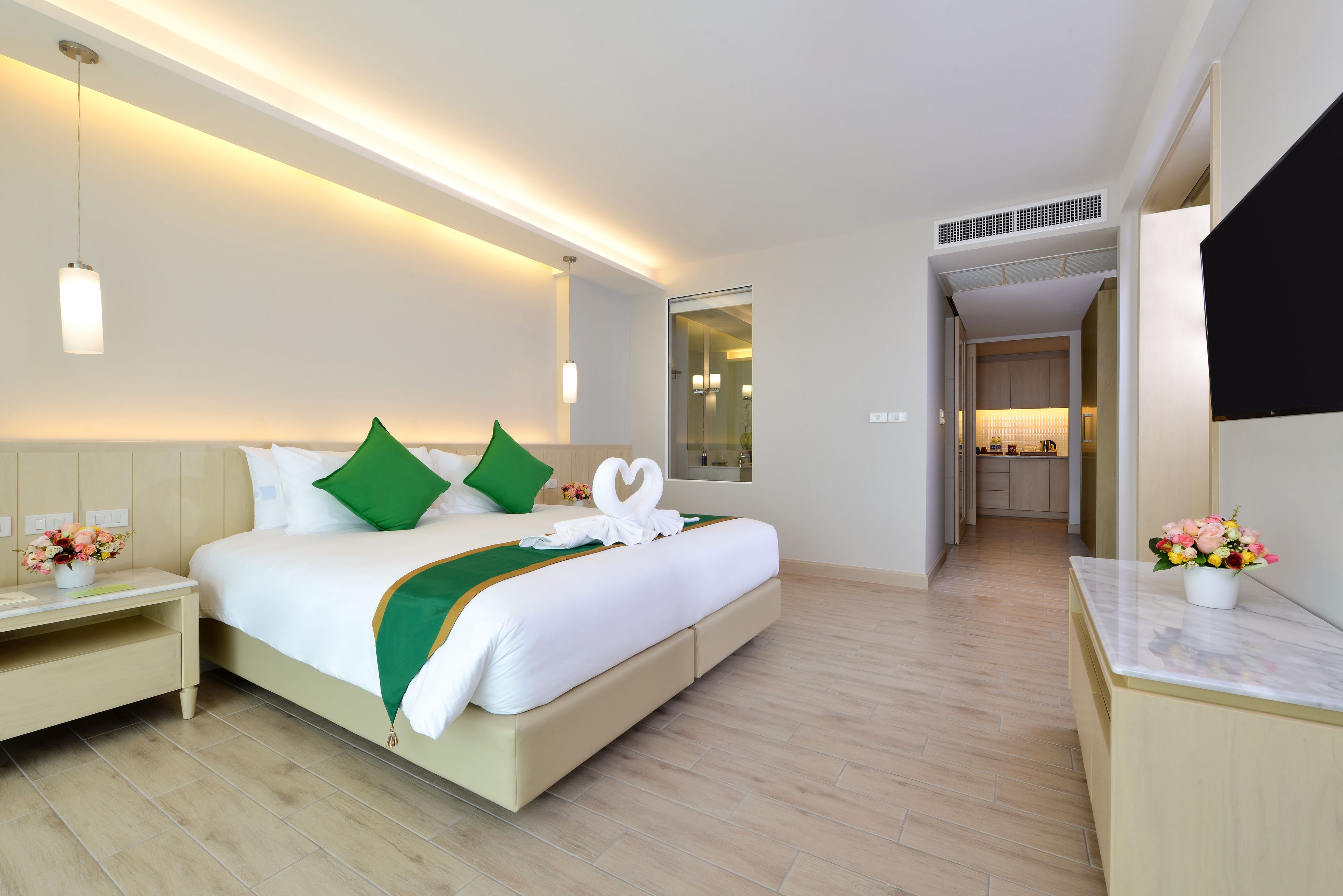 A modern hotel room with a large bed, a bedside table, a nightstand, and a small desk. There is a mirror above the bed and a TV on the wall.