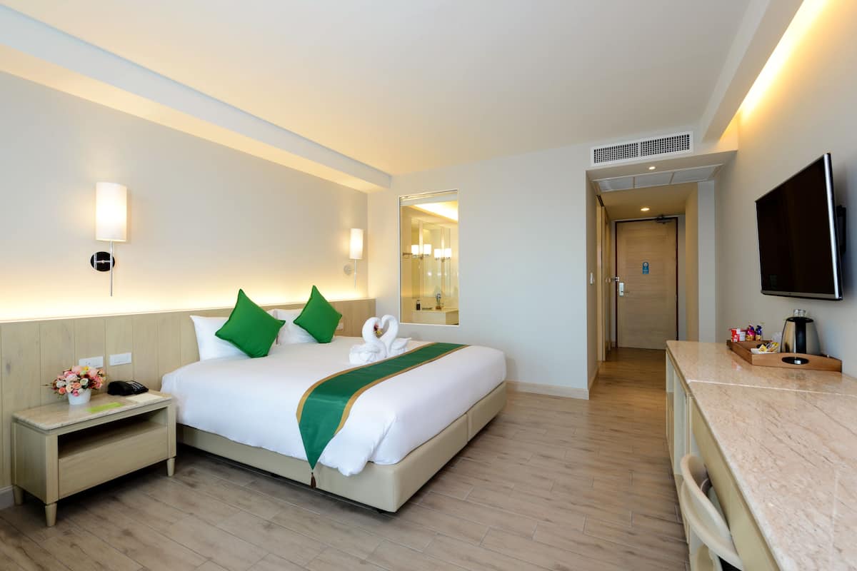 A hotel room with a bed, bedside table, TV, and a mirror.