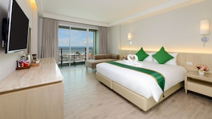 Une chambre d’hôtel comprenant un lit, un bureau, une télévision, un balcon avec vue sur la mer et une table de chevet avec une lampe.
