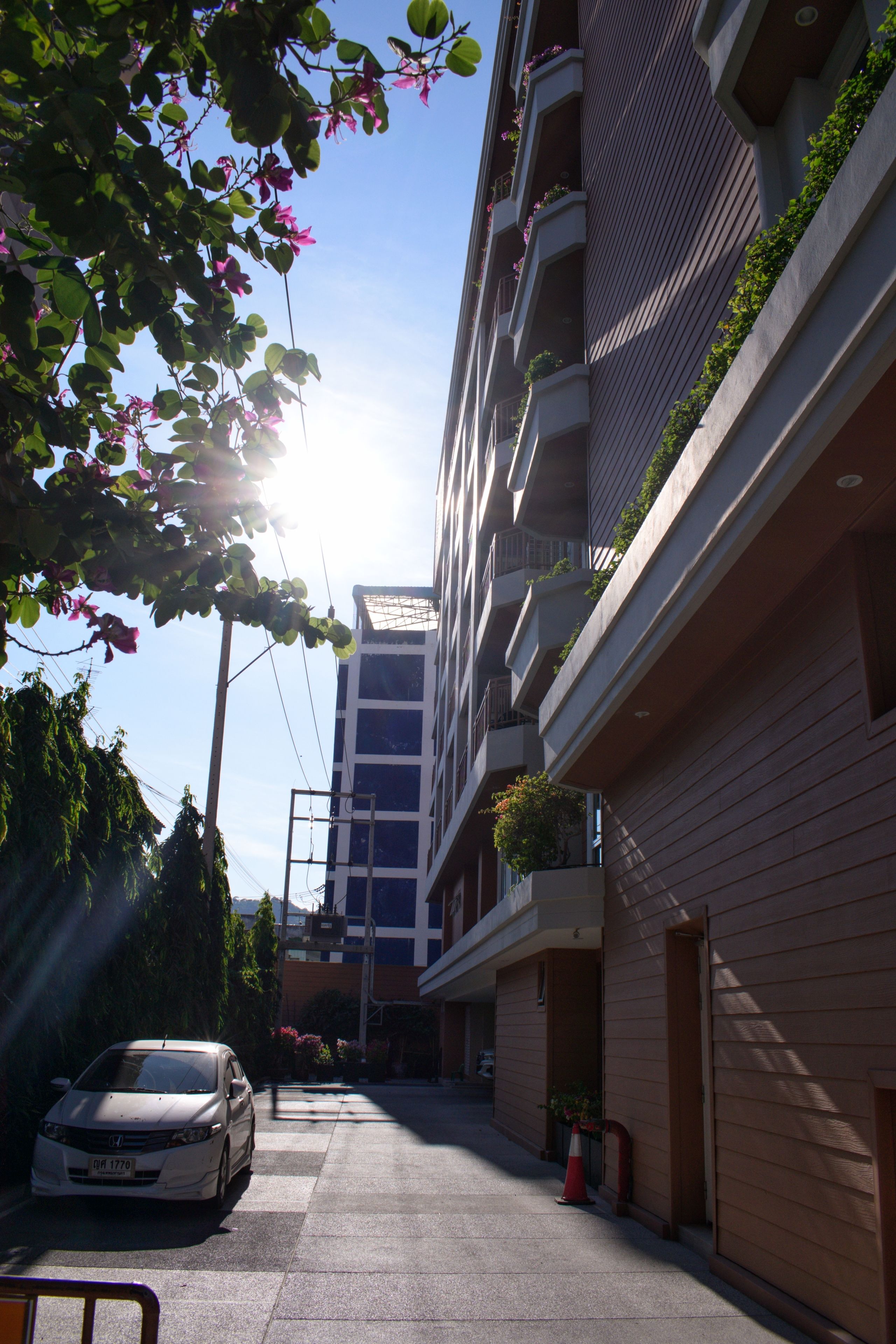 Eine schmale Stadtstraße mit einem parkenden Auto, einem Gebäude mit Balkonen und blauem Himmel.