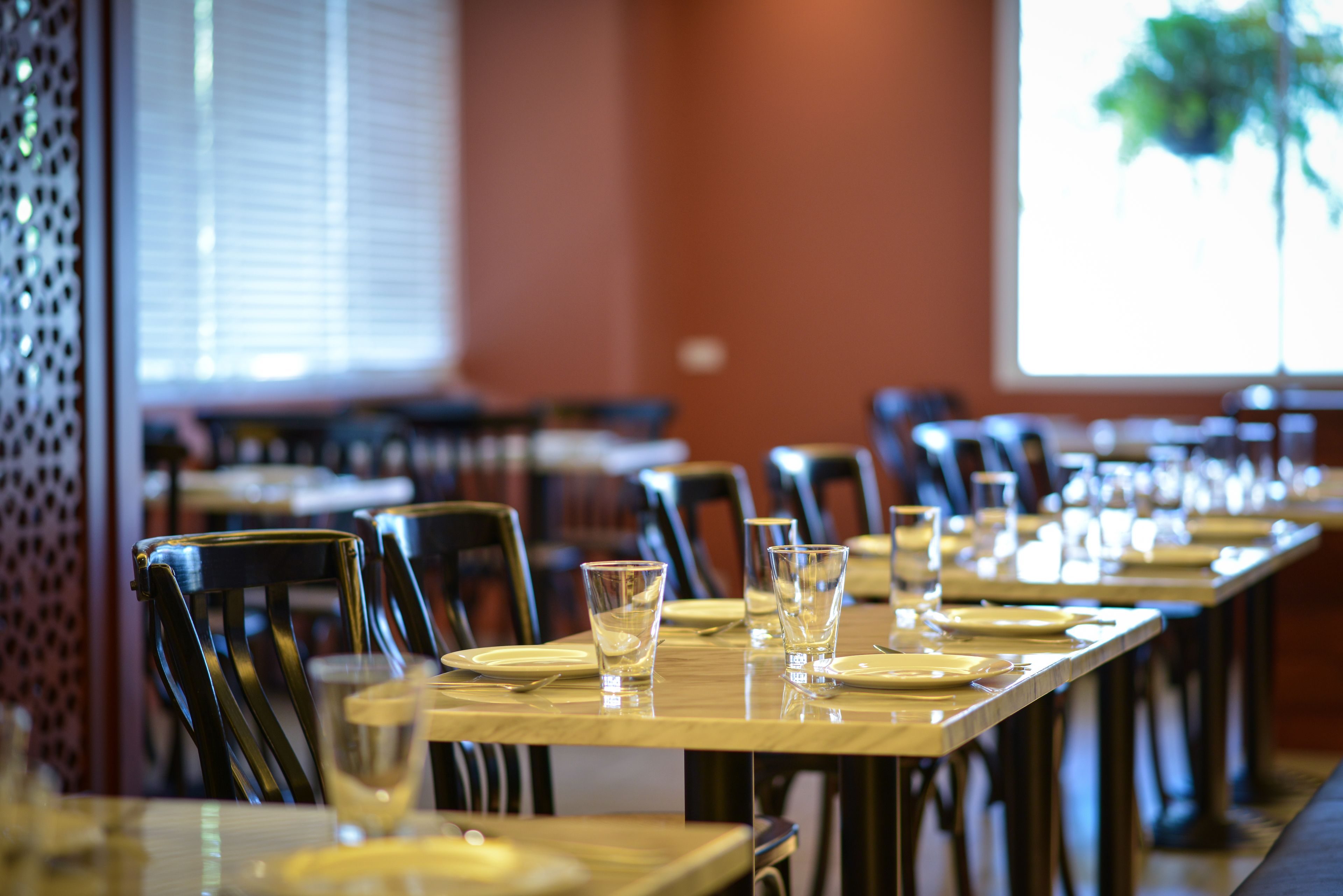 A dining area with tables set for service, chairs, and a window with blinds.
