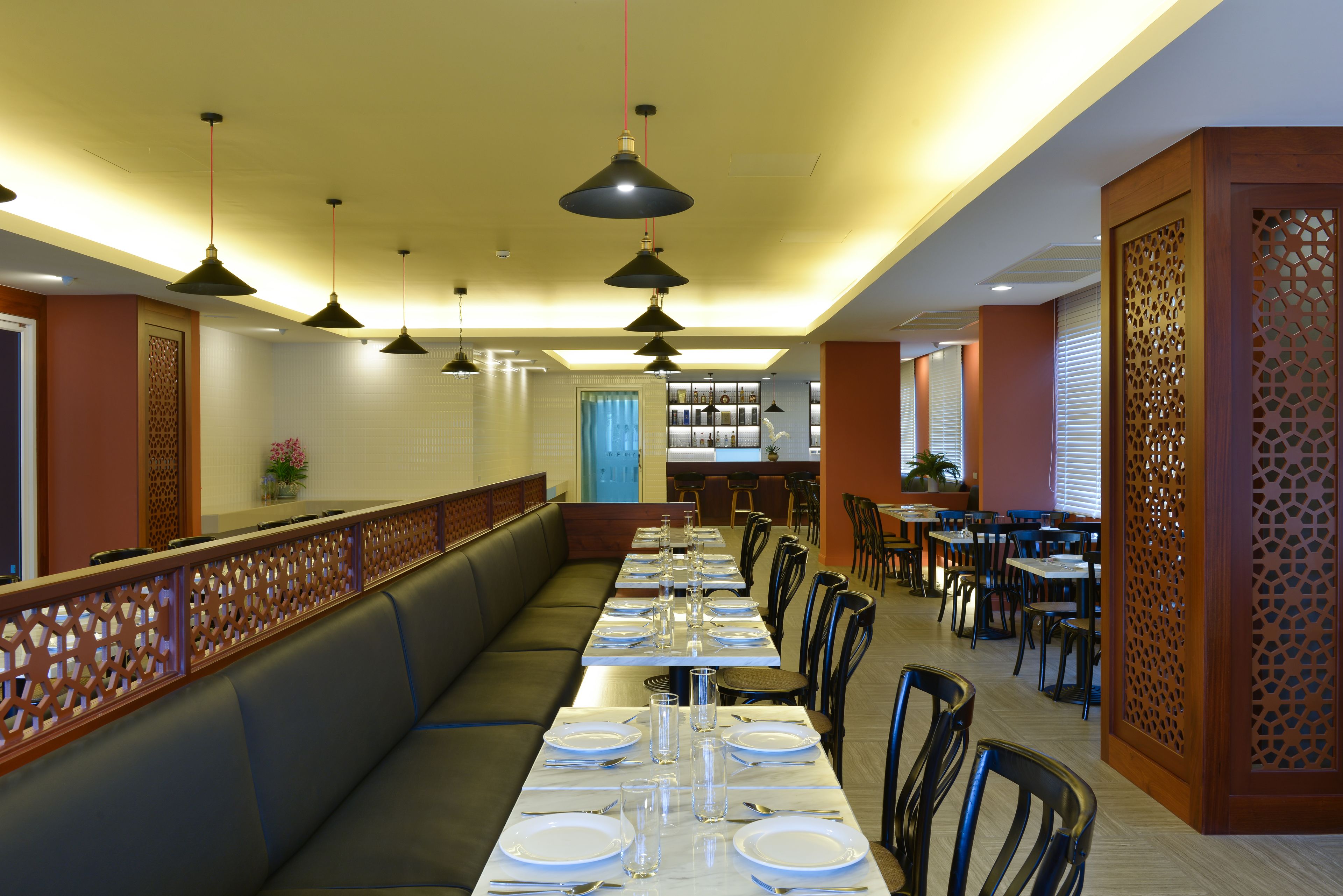 Un restaurante con una larga mesa de comedor dispuesta para una comida, múltiples lámparas colgantes y un panel de madera con diseños intrincados recortados.