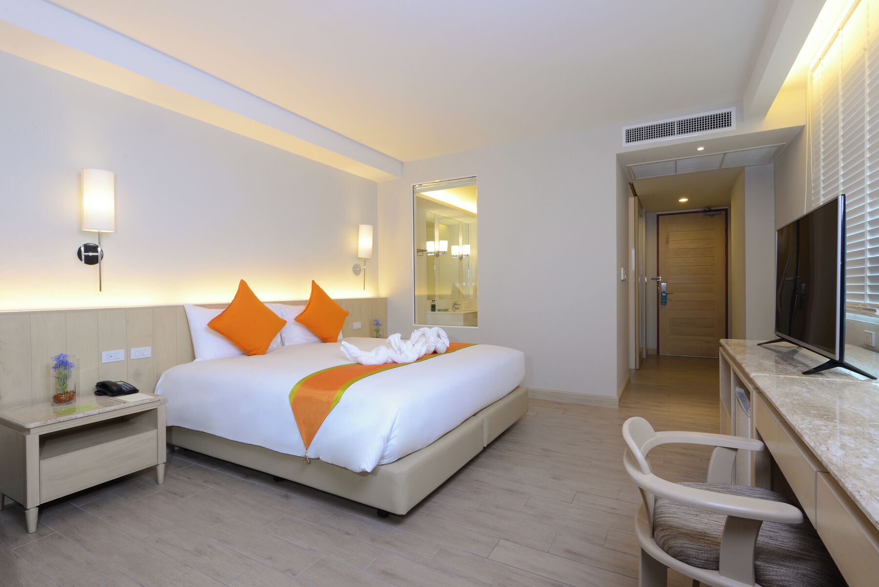 Quarto de hotel com cama, mesa de cabeceira, televisão e uma cadeira.