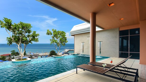 Un espace aménagé au bord de la piscine, avec un fauteuil de relaxation, une table avec une boisson et une vue sur l’océan.