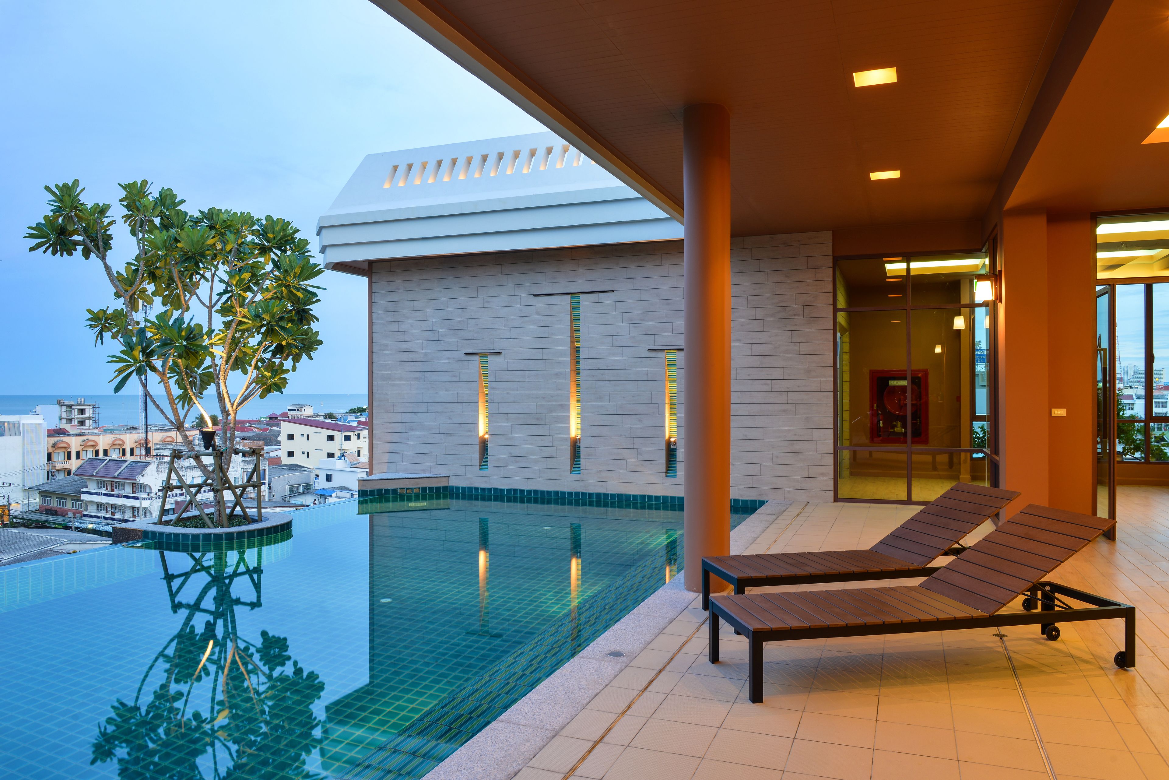 A modern pool area with lounge chairs, a tree, and a building with a glass facade.