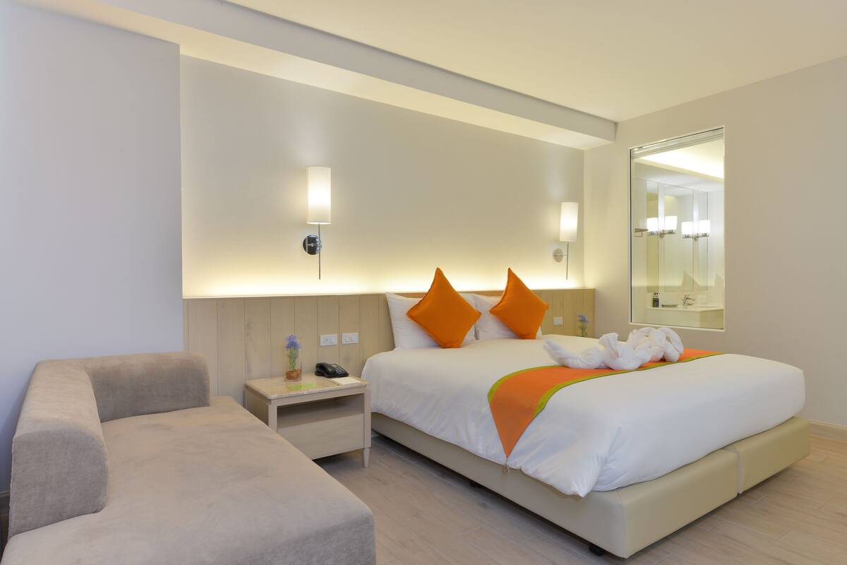 A modern hotel room with a large bed, a bedside table, a chair, and a mirror.