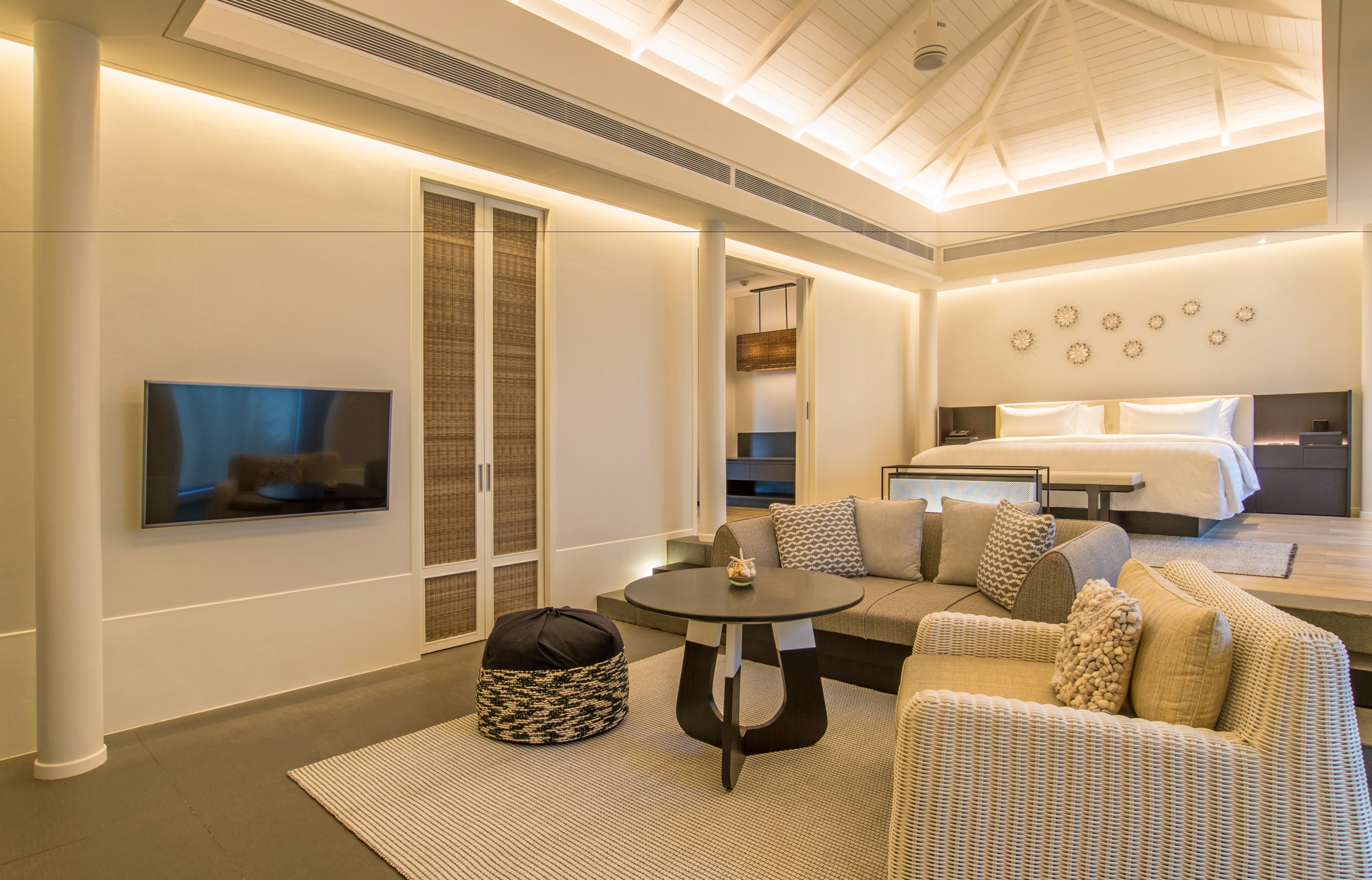 A modern hotel room with a large bed, a sofa, a TV, and a dining table.