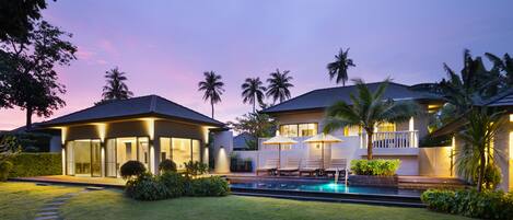 Una casa moderna con piscina, mobiliario exterior y palmeras.