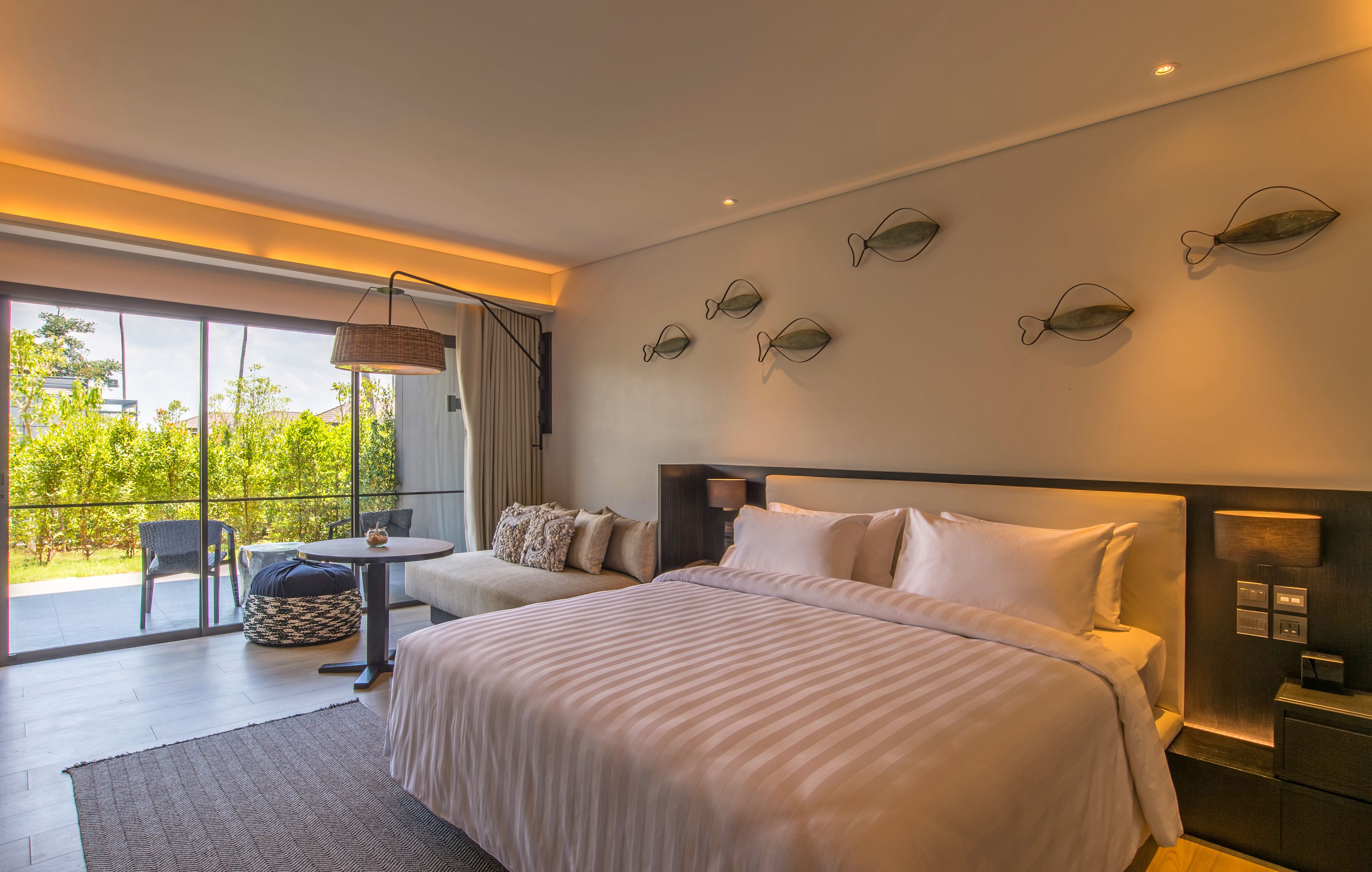 Een moderne hotelkamer met een groot bed, een slaapbank, een eettafel en een balkon met uitzicht op groen.