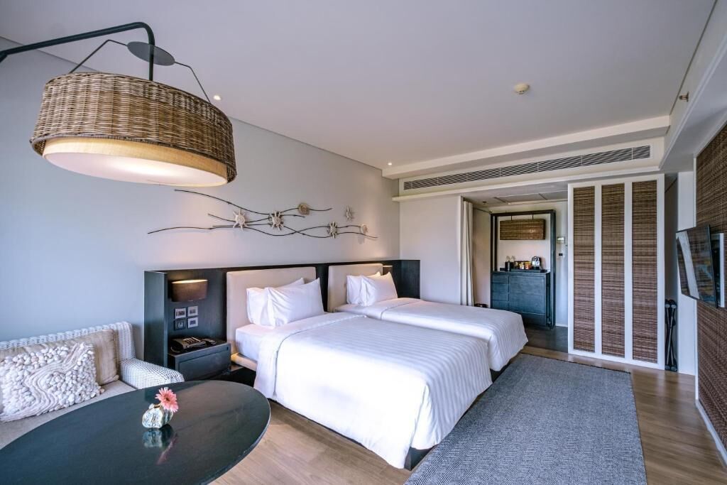 A modern hotel room with two beds, a sofa, a coffee table, and a television.