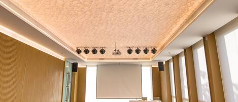 A conference room with patterned ceiling, rows of chairs, and a projector screen.