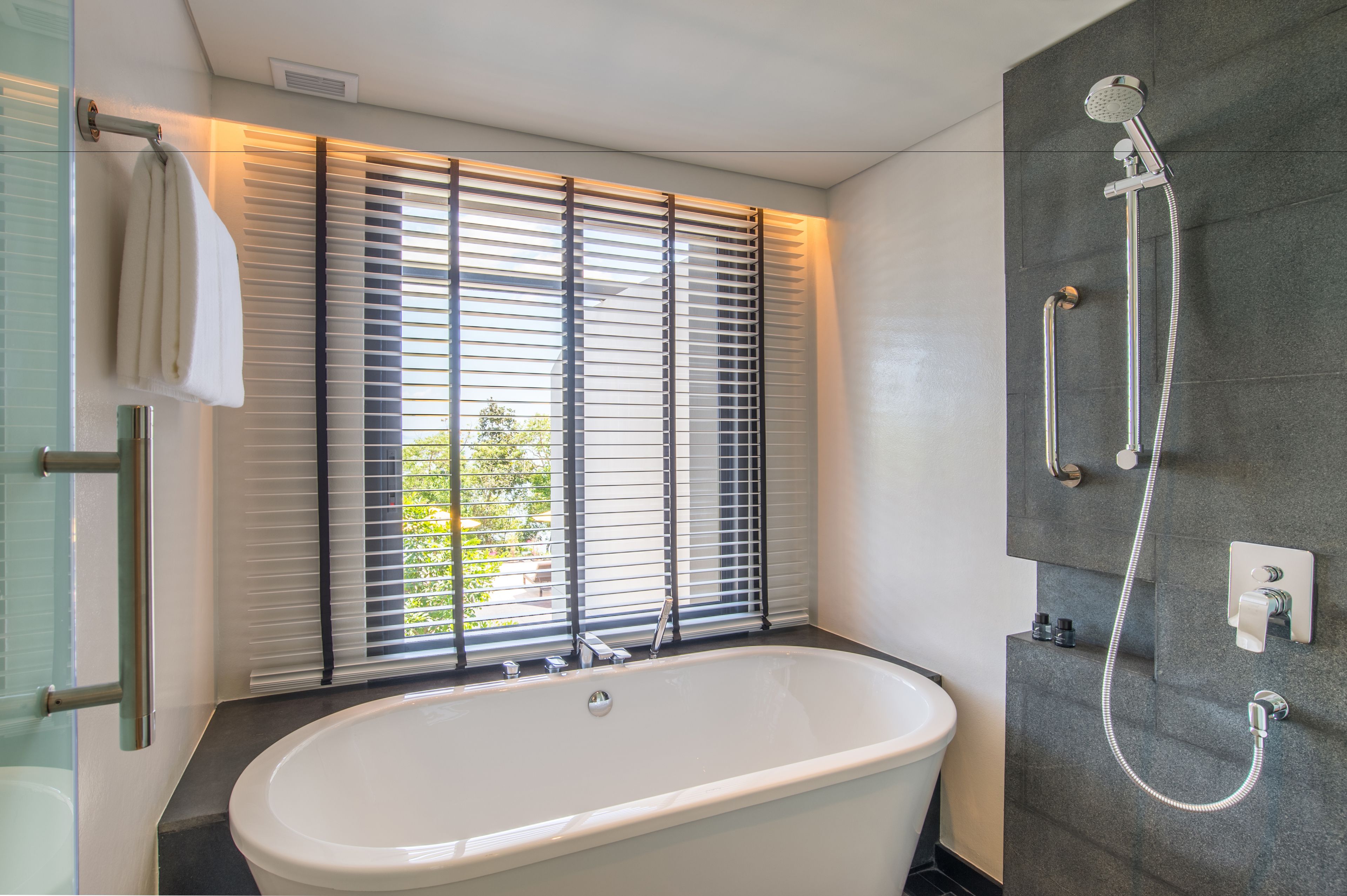 Un baño moderno con una bañera independiente, ducha con cabezal de mano y ventana con persianas.